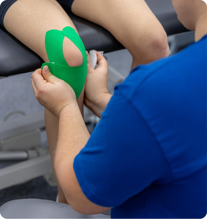 Clinician applying green kinesiology tape around a patient’s knee